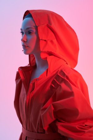A fashion model girl posing in a stylish orange jacket with wide sleeves and a hood. Studio shot...