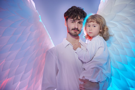 A male guardian angel holds a little baby girl in his arms and protects her. Heavenly mixed light.の写真素材