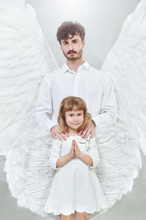 A male guardian angel and a small baby angel girl. White studio background. The concept of peace, hope and goodness.の写真素材