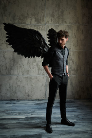 A handsome male Black Angel stands against a grunge wall.の写真素材