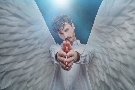 The male guardian angel holds out his hands to the camera with calm and hope in his eyes. Heavenly light surrounds him.の写真素材