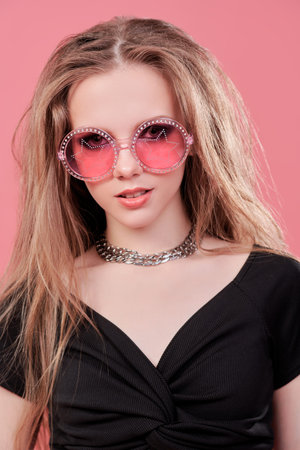 Youth fashion and lifestyle. Youth pop and rock culture. Glamorous teenage girl with bright makeup and rock-style hair styling poses against a pink studio background.の写真素材