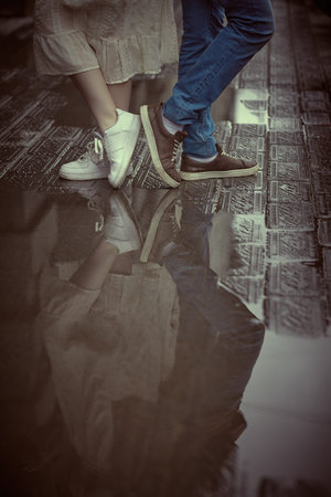 Portrait of the legs of man and a girl and their reflection in the puddle standing with their backs...