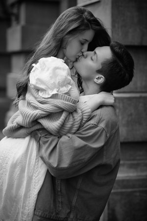 Romantic lovers guy and girl gently kiss and hug each other, standing on a city street. People and...