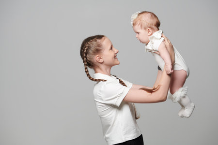 The older sister plays with her younger newborn sister. Studio portrait on a light gray background. Happy children and family. Place for text.の写真素材
