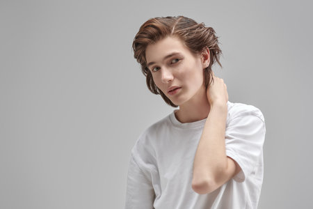 People, emotions. Portrait of handsome thoughtful teen boy in white t-shirt looking at camera. Gray background with place for text. School, education. Modern lifestyle.の写真素材