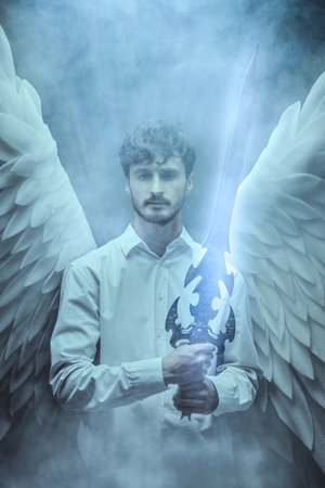 The male guardian angel holds a sword and looks to the camera with calm in his eyes. Heavenly light and haze around him.の写真素材
