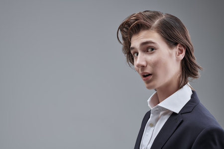 People and emotions. Portrait of a teenage boy in a classic suit, who expresses surprise. Gray studio background with copy space. Modern education.の写真素材