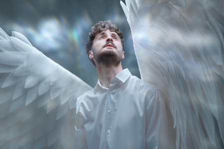 The male guardian angel looks up with calm and hope in his eyes. Heavenly light surrounds him.の写真素材