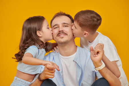 A happy father with his beloved son and daughter, kissing him. Happy family concept. Portrait on a yellow studio background.の写真素材