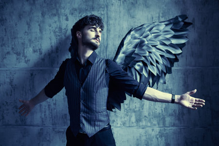 A handsome male Black Angel stands against a grunge wall. Blue moonlight.の写真素材