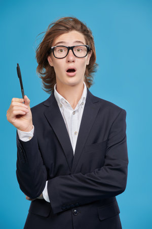 A high school student boy in a suit and glasses is surprised with an idea. Studio blue background. Education.の写真素材