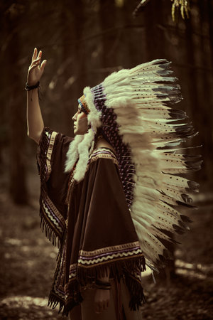A red Indian shaman woman performs a ritual while standing in a wild forest. American ethnic culture. Retro style portrait.の写真素材