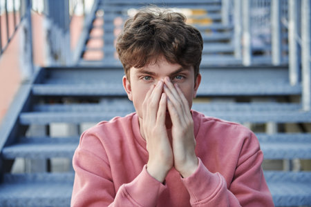 A modern young man sits pensively on a metal staircase on a city street. People, emotions. Life...