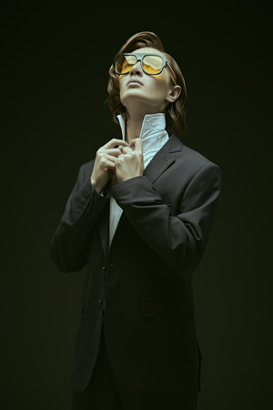 A well-groomed young man with stylish hair styling, posing in an elegant black classic suit, white shirt, a tie and big sunglasses. Black background. Men's fashion and style.の写真素材