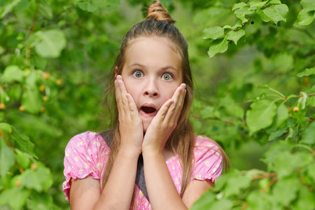 Children's emotions. A funny girl child peeks out from behind the trees and is very surprised.の写真素材