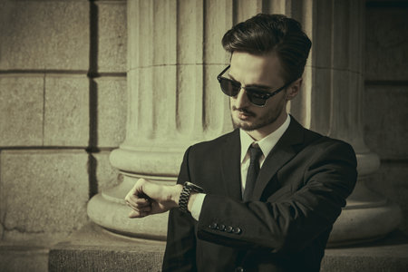 Men's fashion and business style. Portrait of a male fashion model posing in an elegant black suit with a white shirt and tie, wearing black sunglasses on a city street.の写真素材