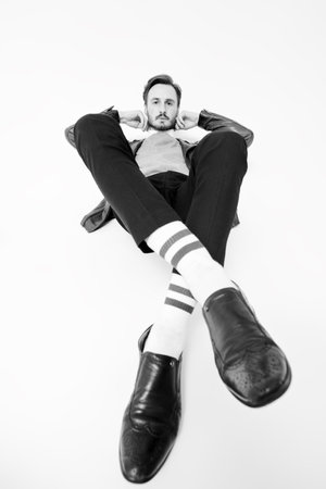 Full length black and white portrait of handsome confident man in black trousers and black leather jacket posing at studio. White background. Fashion for men.の写真素材