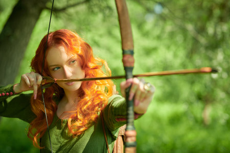 Beautiful and brave young woman archer with magnificent long red hair in a historical celtic dress...