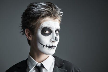 A teenage boy in a costume of skeleton posing at studio on a grey background. Halloween party for teenagers. Space for text.の写真素材