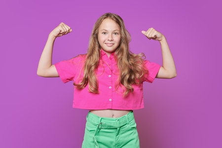 Children's emotions. Cheerful emotional girl posing in a fashionable bright pink blouse and green jeans on a purple studio background. Children's summer fashion.の写真素材