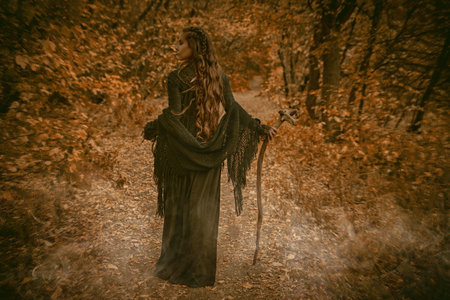 A shaman woman in black garment stands in an autumn forest with a shaman's staff in her hand. Ethnic culture. Shamanic rituals.の写真素材