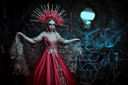 Dia de los Muertos. Sugar skull girl. Beautiful Santa Muerte in a festive rich golden-red dress and floral headdress stands in the old castle. Day of The Dead. Halloween.の写真素材