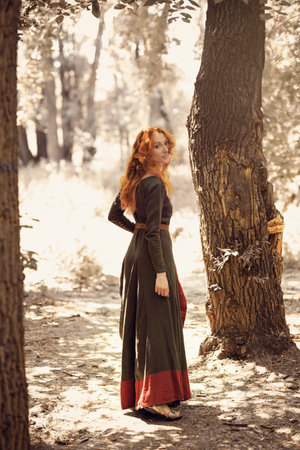 Fantasy world. Portrait of a beautiful red-haired girl of the Middle Ages walks in a summer forest....