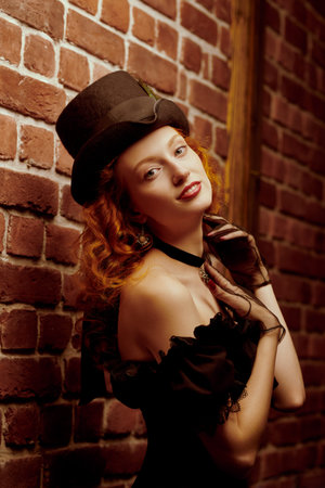 Portrait of a beautiful romantic girl with curly red hair, dressed in elegant black dress with a...