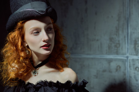 The heroine of a novel of the 19th century. Portrait of a pretty and confident adventurous girl with bright red hair, dressed in an elegant black dress with a decollete and a felt hat. Place for text.の写真素材