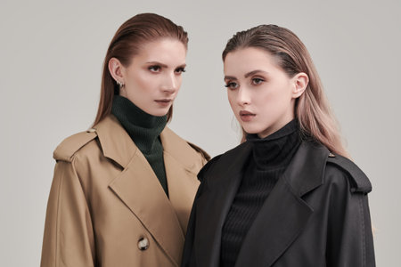 Two stylish beautiful girls fashion models posing in trendy trench coats on a white studio background. Women's fashion and beauty.の写真素材