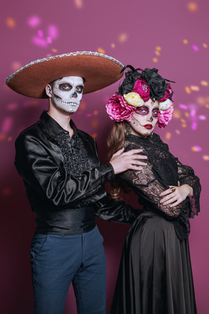 A merry Halloween and Day of the Dead celebration. A couple of young people in costumes and make-up of a sugar skull and Calavera Catrina pose against a festive background.の写真素材