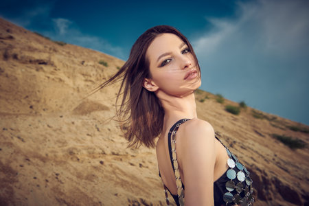 Summer female beauty and hot vacation. Beautiful brunette girl posing in a black bikini and a mesh dress sparkling in the sun against the background of the sands and blue sky.の写真素材