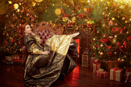 Christmas fairy tales about princesses. A beautiful red-haired princess in a rich brown and gold dress rests in the castle, fabulously beautifully decorated for Christmas, and waits for a miracle.の写真素材