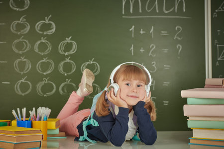 Education. A little first-grader girl lies on her desk surrounded by books and smiles. There is a...