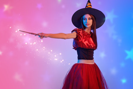 Pretty young witch. Halloween celebration. Portrait of a cute teenage girl posing at studio in a witch's costume and a magic wand in her hand. Mixed colorful lighting. Place for text.の写真素材