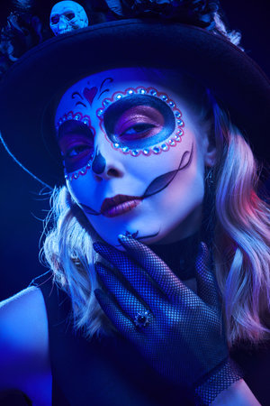 Close-up portrait of a beautiful Sugar Skull girl in a festive colorful lighting. Day of the Dead...