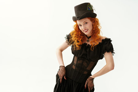 Portrait of an attractive flirty girl with curly red hair and delicate natural makeup, dressed in an elegant dress and felt hat in the style of the 19th century. White background with space for text.の写真素材