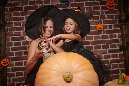 Halloween holiday. Mom and daughter in witch costumes are preparing to celebrate Halloween with pumpkins and a magic ball.の写真素材