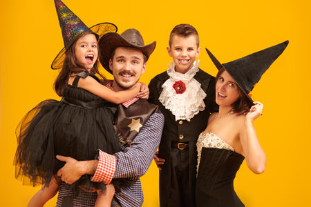 Happy Halloween! Portrait of a cheerful family of parents and children dressed in carnival costumes is having fun celebrating Halloween. Yellow studio background.の写真素材