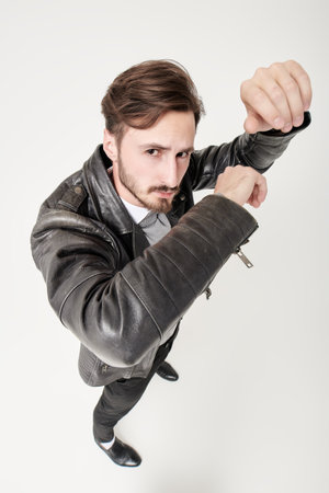Full length portrait of handsome confident man in black trousers and black leather jacket posing in motion at studio. White background. Fashion for men.の写真素材