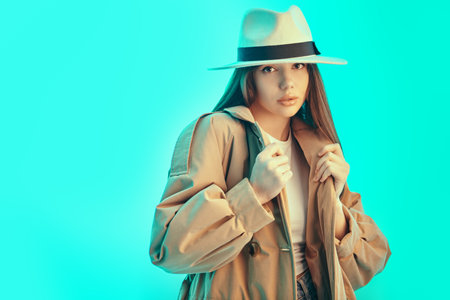 Beauty portrait. Portrait of a beautiful brunette girl wearing a fashionable brown trench coat and a white felt hat, looking confidently at the camera. Fashion, demi-season clothing and accessories. Place or text.の写真素材