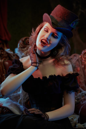 A beautiful and treacherous female vampire sits in an armchair of an old castle and bares her bloodied fangs. Vampire novels. Vintage style. Halloween.の写真素材