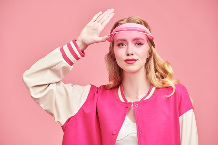 A beautiful blonde fashion model girl posing in a pink visor and a pink bomber jacket on a pink studio background. Youth girlish sports style.の写真素材