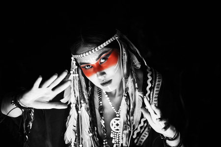 Black-and-white photo with colour accent. American ethnic culture and history. Portrait of a beautiful American Indian girl in traditional dress and jewelry on a black background.の写真素材