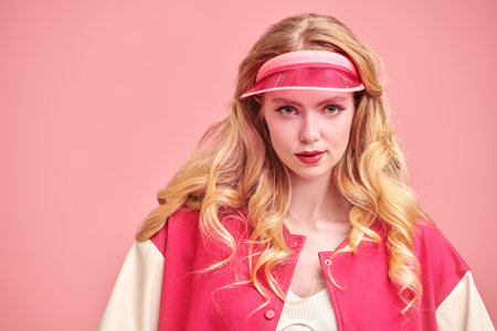 Trendy pink color. A beautiful blonde  girl poses in a pink visor and a pink bomber jacket on a pink studio background. Copy space. Youth girlish sports style.の写真素材