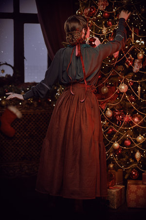 Vintage Christmas. A joyful aristocratic lady decorates the fir tree in a Christmas room. The heroine of the novel of the 19th - early 20th century. Happy Christmas time.の写真素材