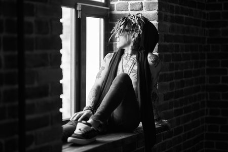Black and white portrait of a cool rock musician looking to the window from a room with brick walls....