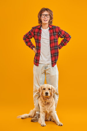 A modern teenager boy in casual clothes is together with his best friend, his dog. Yellow studio background. People and emotions. Pets.の写真素材