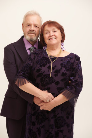 A happy elderly married couple in fashionable evening dresses tenderly hug each other. White studio...
